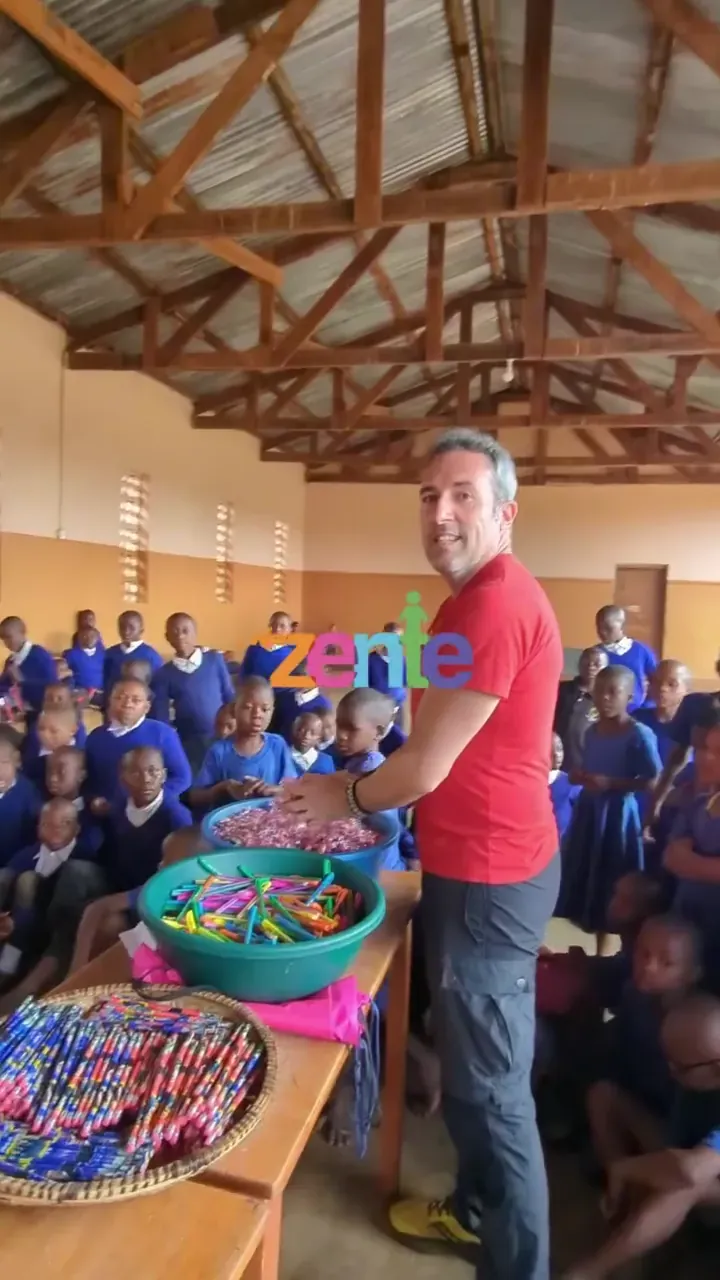 Un volontario di Zente in una scuola in Tanzania, davanti a una sala piena di bambini e a ceste di matite colorate